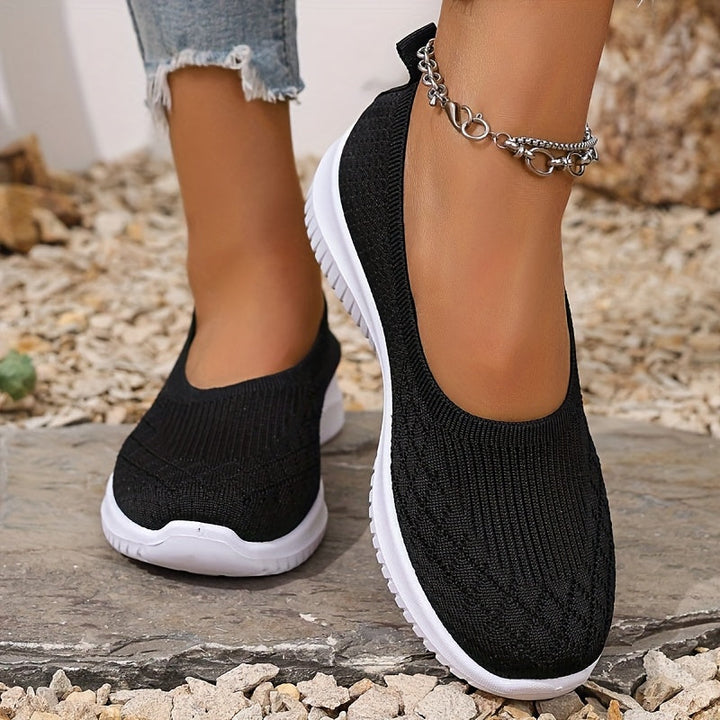 Close up of a model wearing black breathable mesh flats with white soles and a silver ankle bracelet
