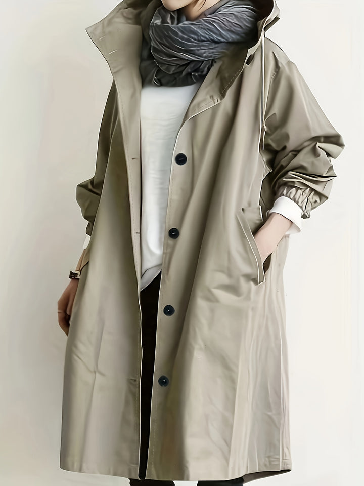 Side view, model wearing an elegant woven trench coat in a light taupe shade with black buttons and a hood