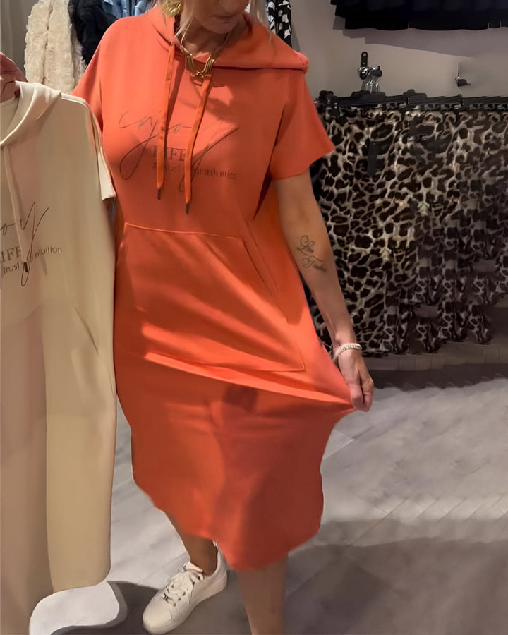 Front view of a model wearing an orange hooded sweatshirt dress, holding up the fabric to show stretch