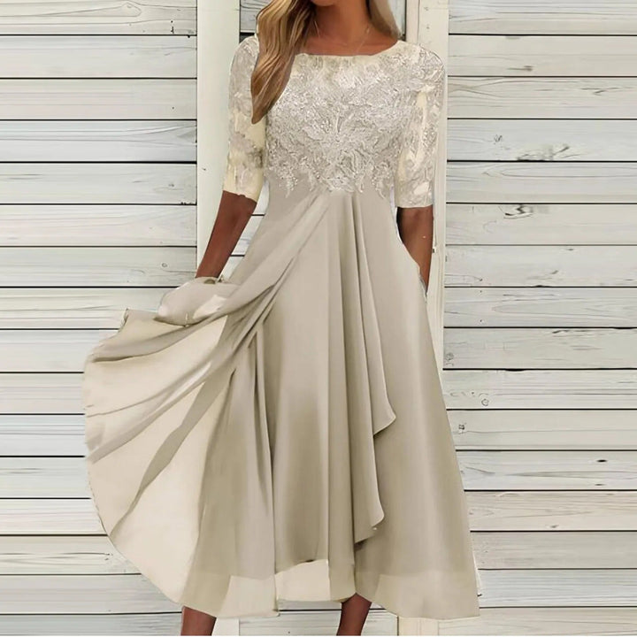 Front view of a model in a beige lace dress with a flowing viscose skirt and sheer sleeves