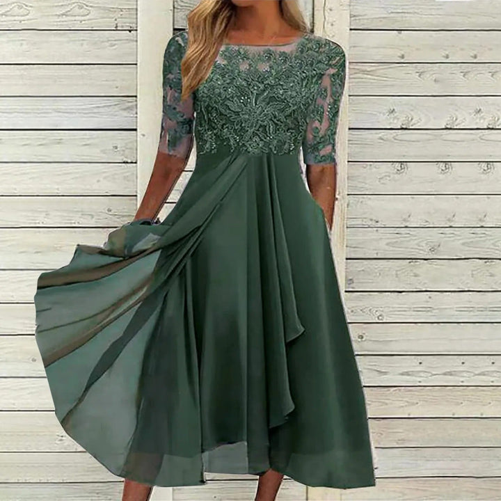 Front view of a model in a green lace dress with a flowing viscose skirt and sheer sleeves