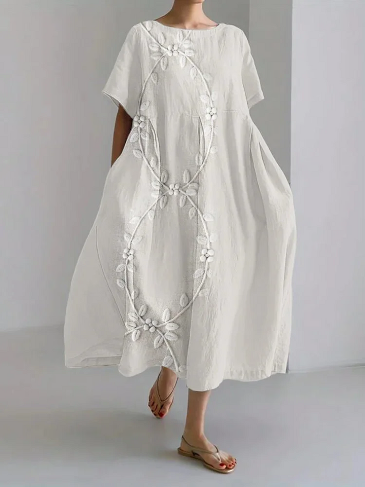 Elegant long dress worn by model, front view, in white linen blend with white vine embroidery design
