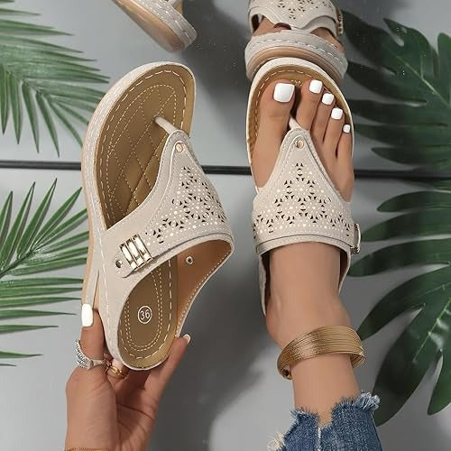 Close up of a model wearing one beige orthopedic leather sandal, holding another to show comfort and detail