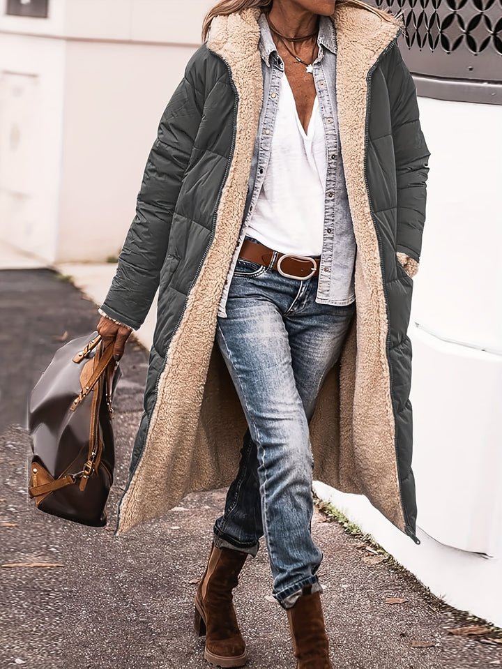 Three quarter view, model in a dark green reversible quilted hooded coat with cream sherpa lining, jeans, and boots