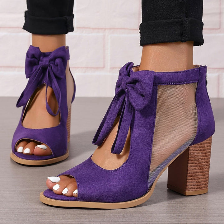 Front view of purple chunky heel open-toe sandals with bows, worn by model