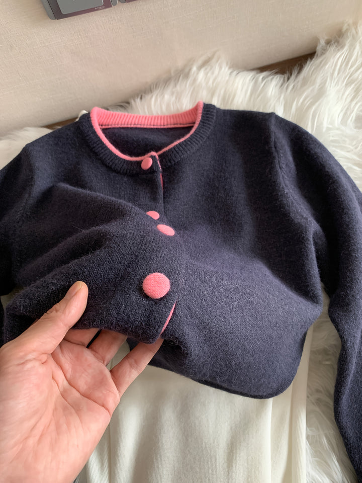 Close up of a hand holding the cuff of a navy knitted buttoned cardigan with pink trim
