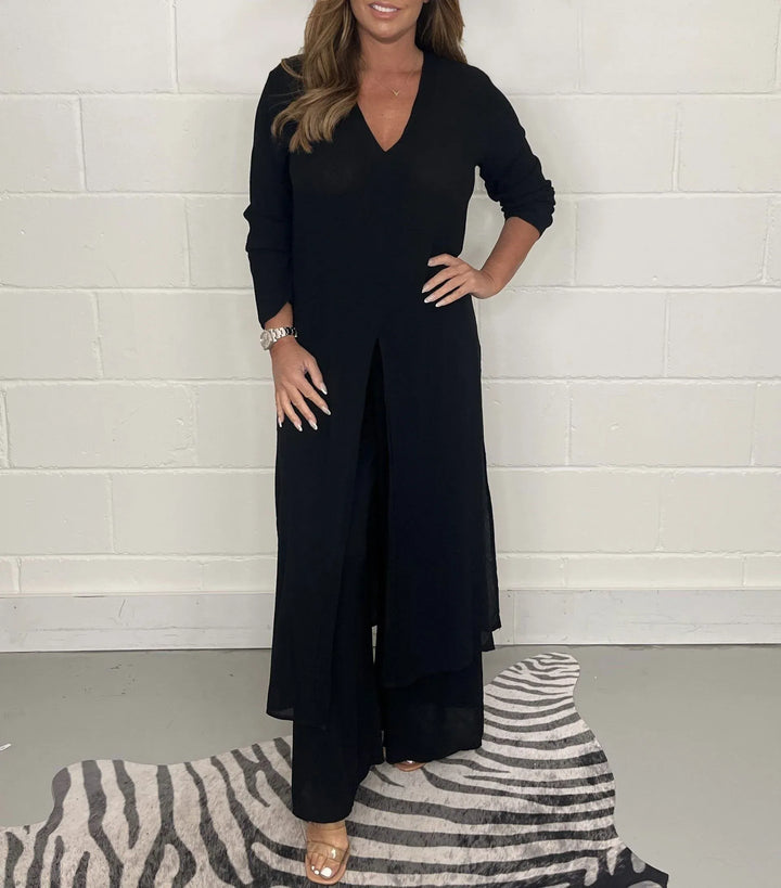 Front view of a model in a black two-piece wide leg jumpsuit set with a long tunic top and v-neck