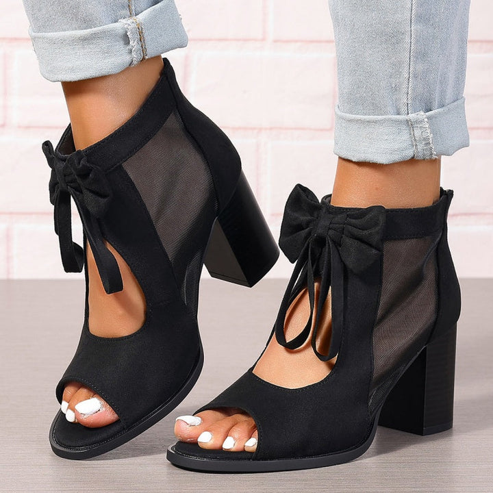Back view of black chunky heel open-toe sandals with bows, worn by model