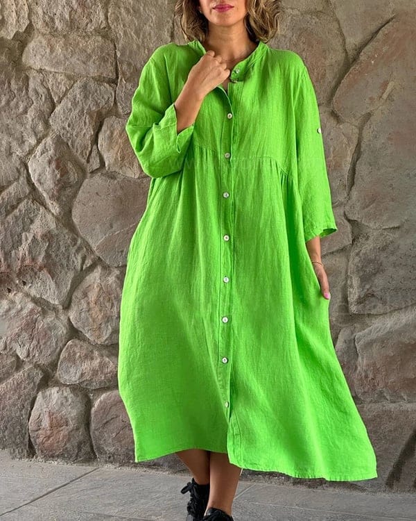 Front view of a model wearing a bright green loose shirt midi dress with white buttons against a stone wall