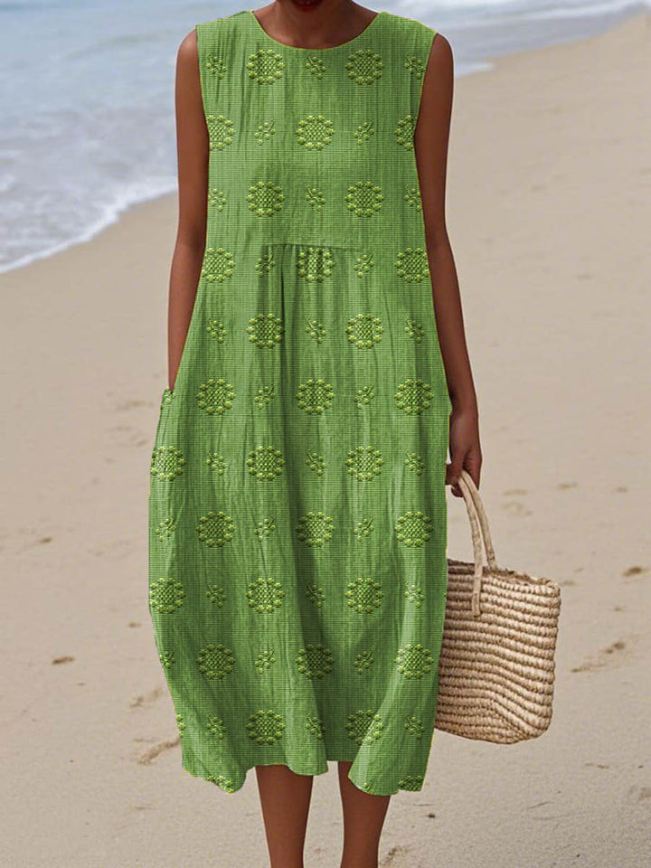Front view, model wearing a green floral print vintage boho dress with a woven bag on a beach