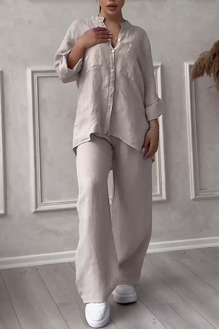 Front view of a model in a beige long sleeve blouse and wide leg pants set with hand on chest