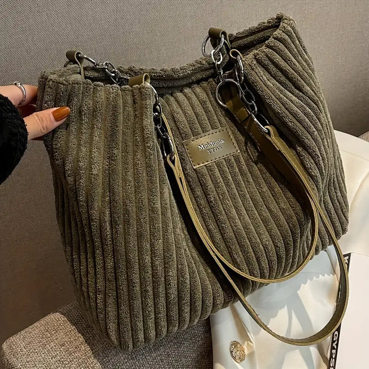 Close up of a green corduroy tote bag with olive straps and silver chain details worn by model