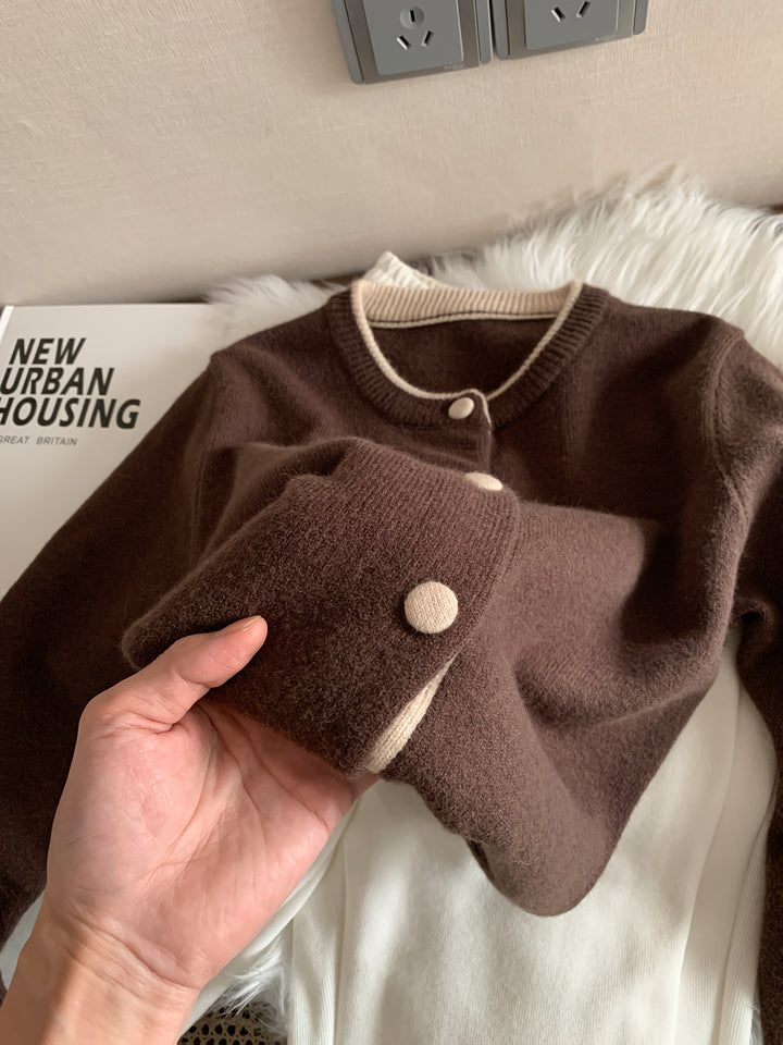 Close up of a hand holding the cuff of a brown knitted buttoned cardigan with cream trim