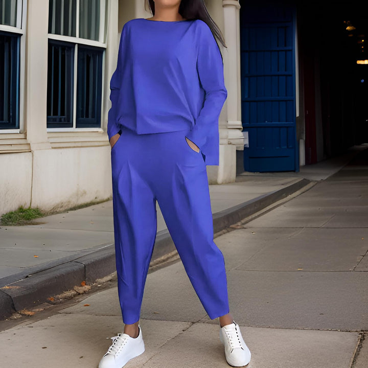 Front view, model wearing a blue loose fit Elena Two-Piece Set, hands in pockets, against a blue wall