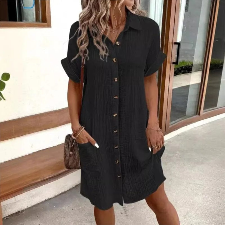 Front view of a model wearing a black collared summer dress with short sleeves, front buttons, and two pockets