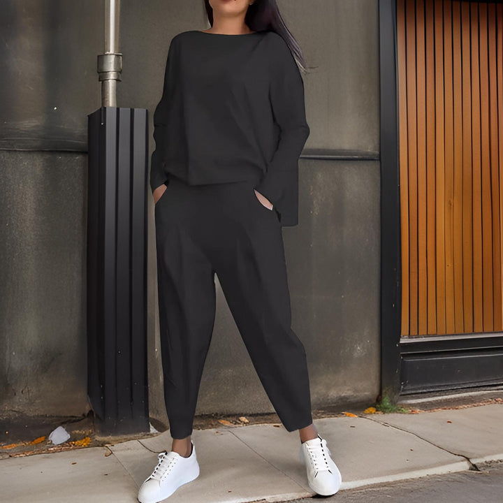Front view, model wearing a black loose fit Elena Two-Piece Set, hands in pockets, wearing white sneakers