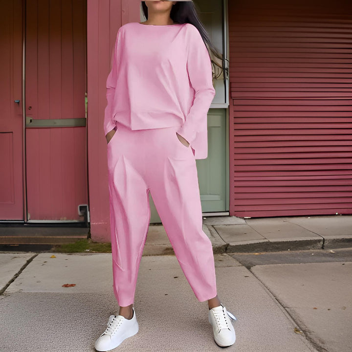 Front view, model wearing a pink loose fit Elena Two-Piece Set, hands in pockets, against a pink wall
