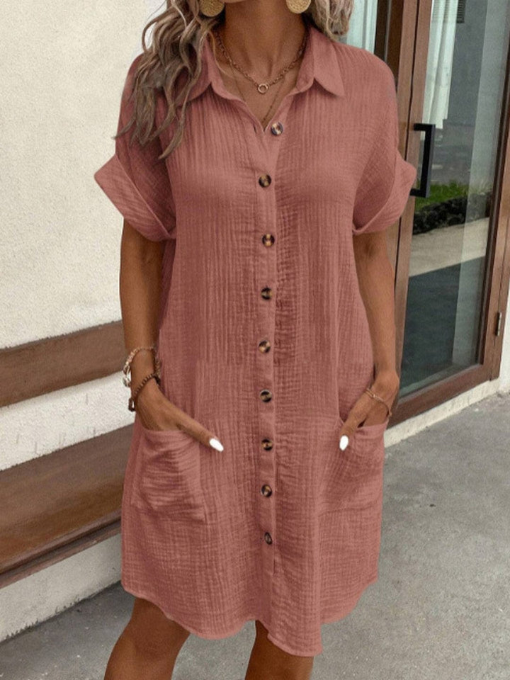 Front view of a model wearing a terracotta collared summer dress with short sleeves, front buttons, and two pockets