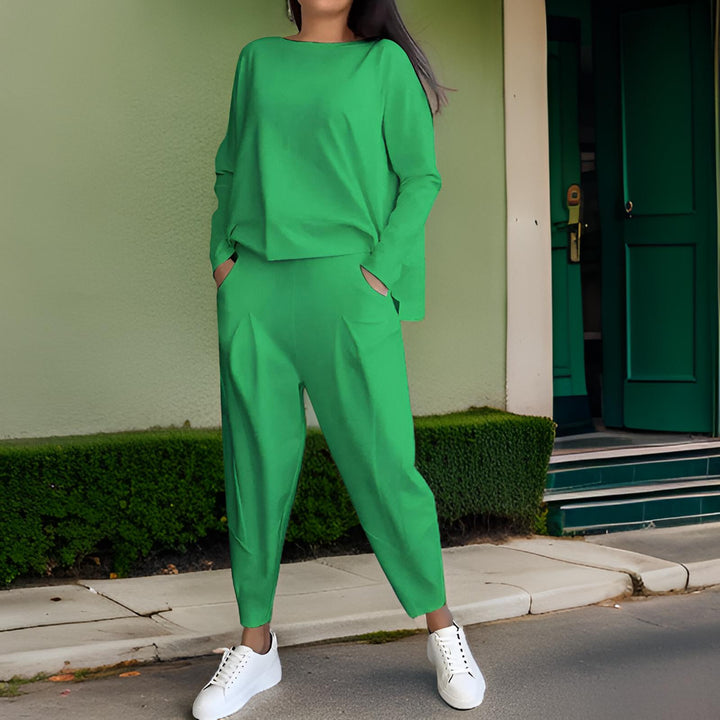 Front view, model wearing a green loose fit Elena Two-Piece Set, hands in pockets, against a green wall