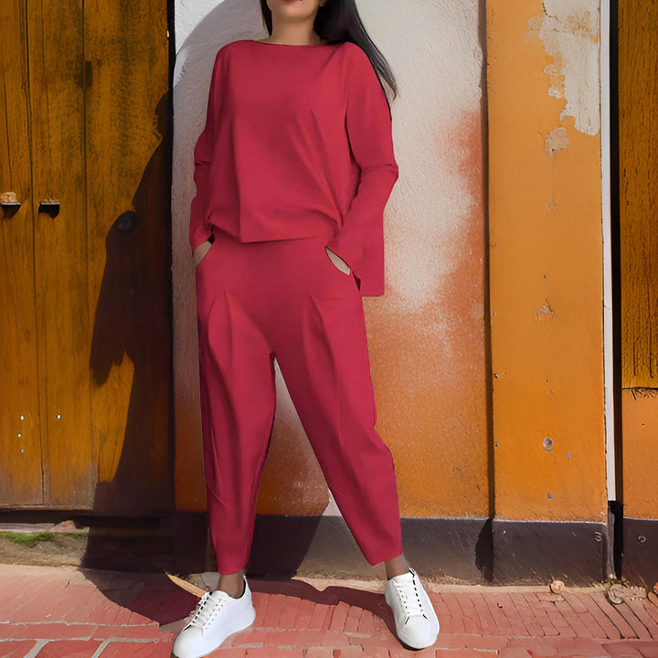 Front view, model wearing a red loose fit Elena Two-Piece Set, hands in pockets, against an orange wall
