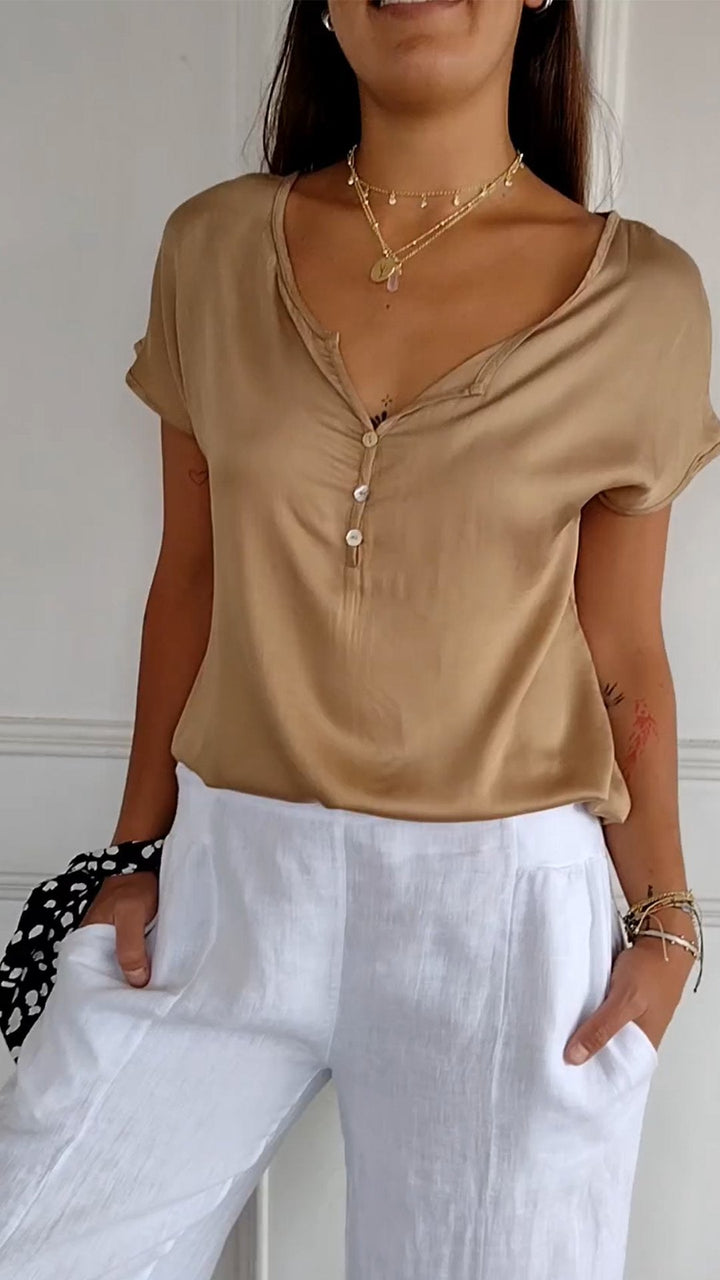 Close up view of a woman wearing a tan V-neck tee with layered gold necklaces