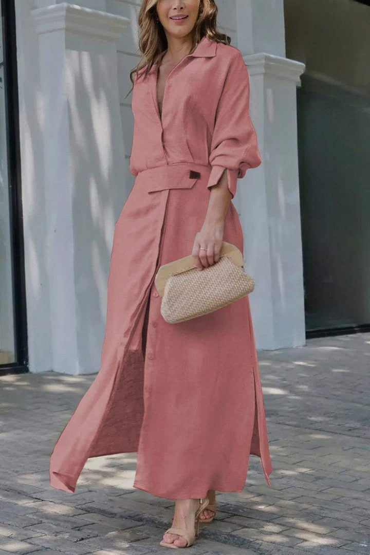 Front three quarter view of a model in a pink solid colour maxi shirt dress with a woven clutch bag and heels