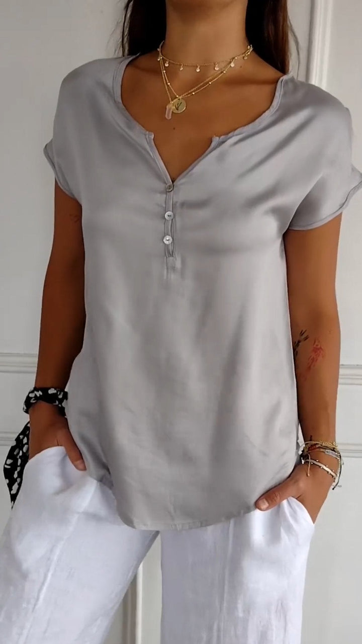 Close up view of a woman wearing a light grey V-neck tee with white buttons and layered gold necklaces