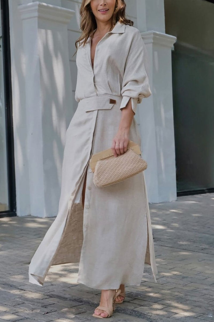 Front view of a model wearing a long sleeve solid colour maxi shirt dress with high slits and a clutch bag