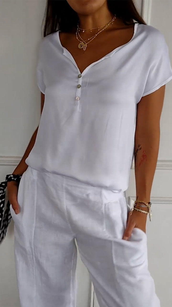 Close up view of a woman wearing a white V-neck tee with white buttons and layered gold necklaces
