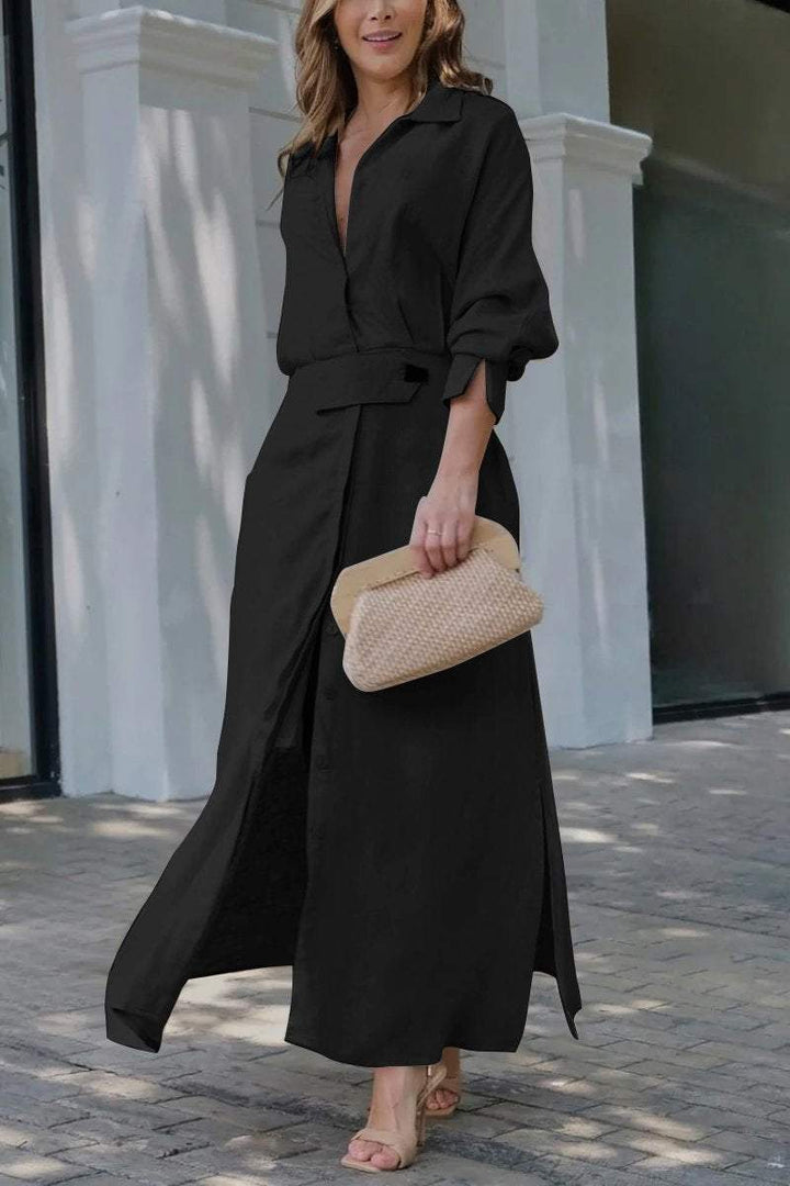 Front view of a model wearing a black solid colour maxi shirt dress with a deep V neckline and high slits