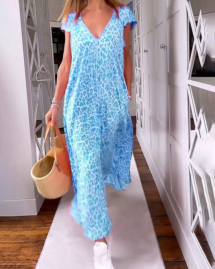 Front view of a model in a blue leopard print maxi dress, walking with a straw bag and white sneakers