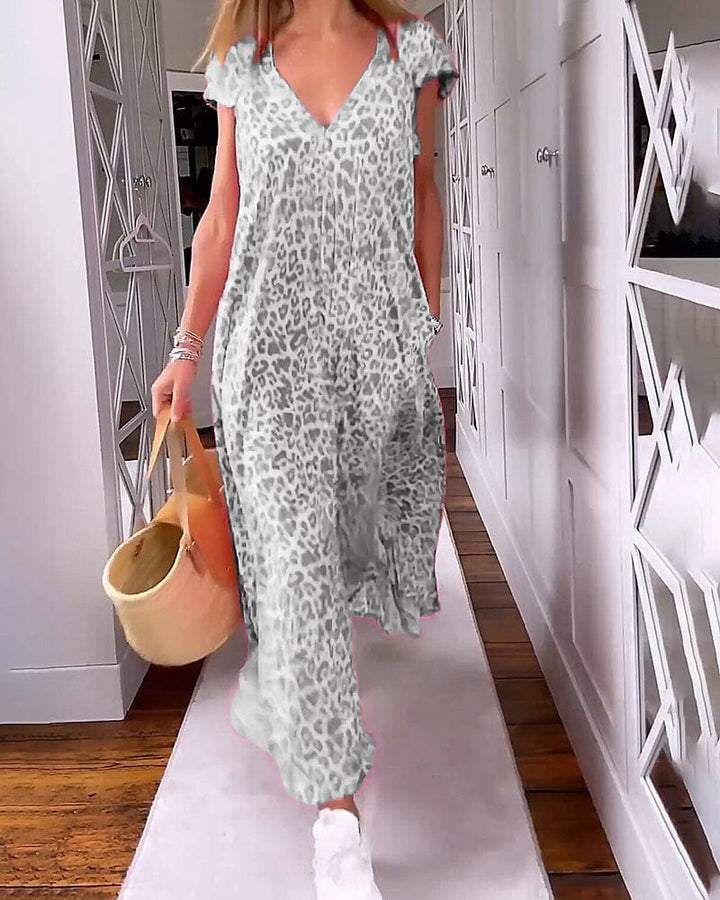Front view of a model in a grey leopard print maxi dress, walking with a straw bag and white sneakers