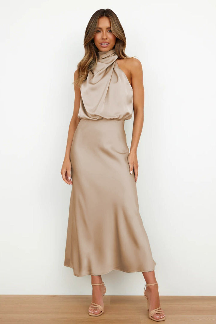 Front view of a model in a beige satin halter neck maxi dress with a relaxed bodice and fitted skirt