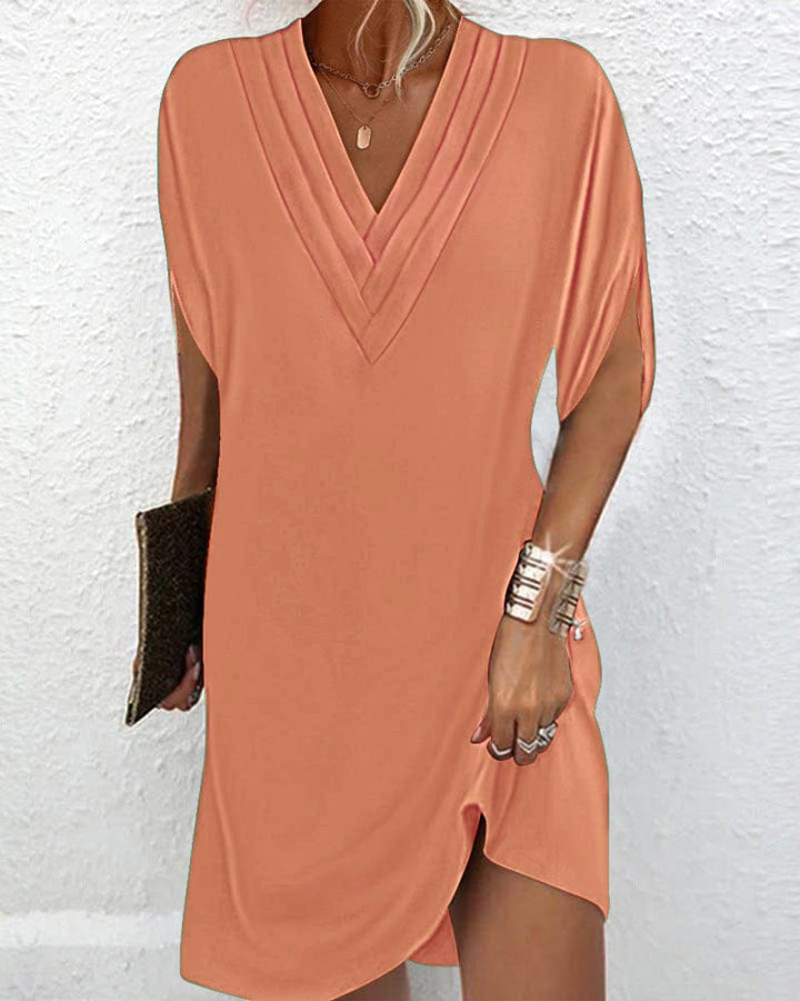 Front view of a model wearing a peach V neck mini dress with batwing sleeves and a silver cuff bracelet