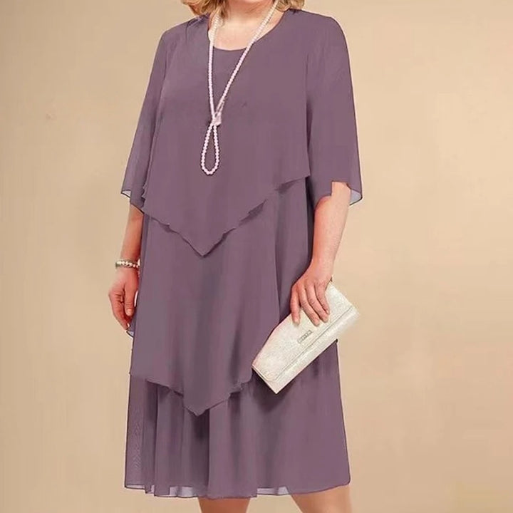 Front view of a woman wearing a layered purple elegant dress with a white pearl necklace and clutch bag
