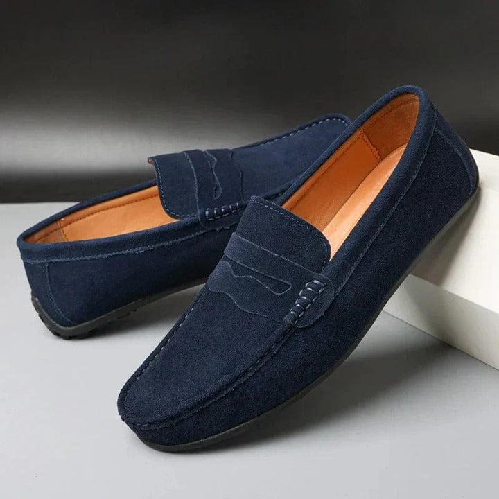 Pair of blue suede loafers, side view, with a black sole and tan interior