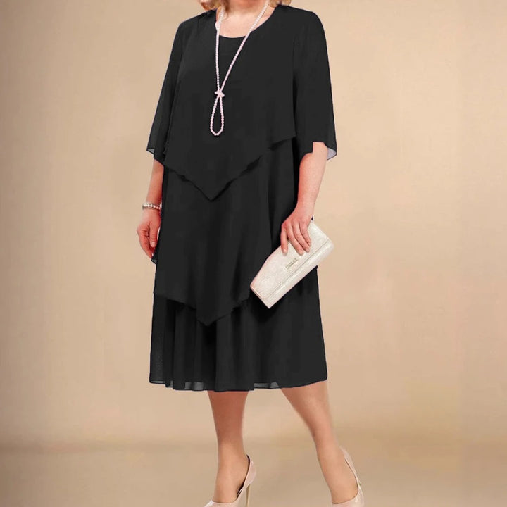 Front view of a woman wearing a black elegant dress with a long pearl necklace, bracelet and clutch bag