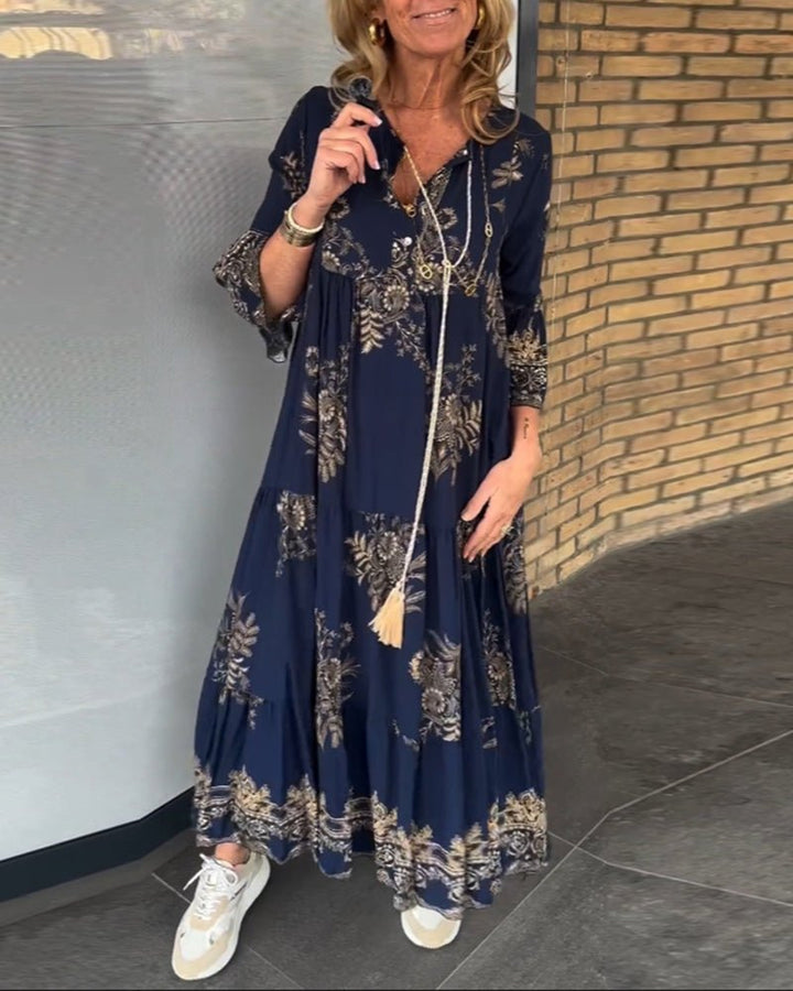 Front view, model wearing a navy vintage flowy dress with gold floral print and a long tassel necklace