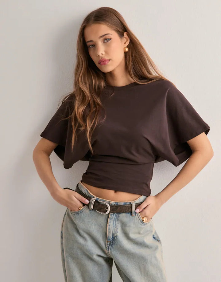 Front view of a model wearing a brown oversized icon tee with wide sleeves and light wash jeans