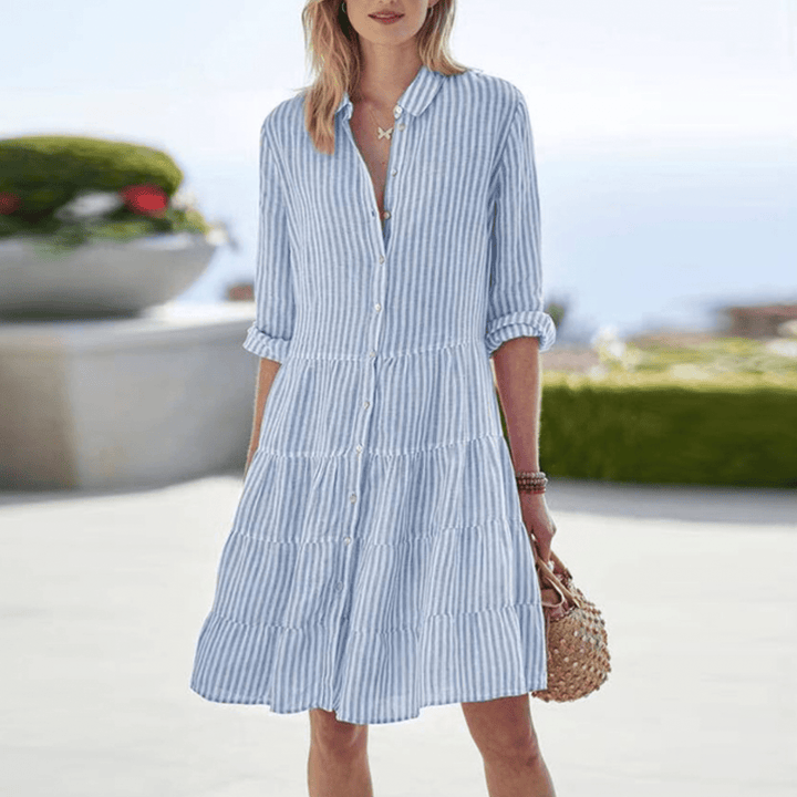 Front view of a model wearing a blue and white striped elegant lightweight shirt dress with a tiered skirt