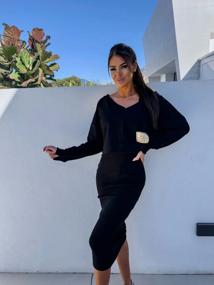 Front view of a model wearing a casual black sweatshirt and dress set with a gold square patch on the top