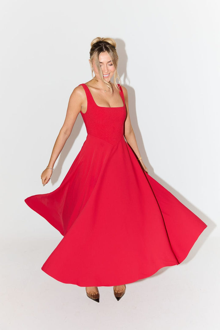 Front view of a model twirling in a red timeless flowy midi dress with a square neckline and a high waist