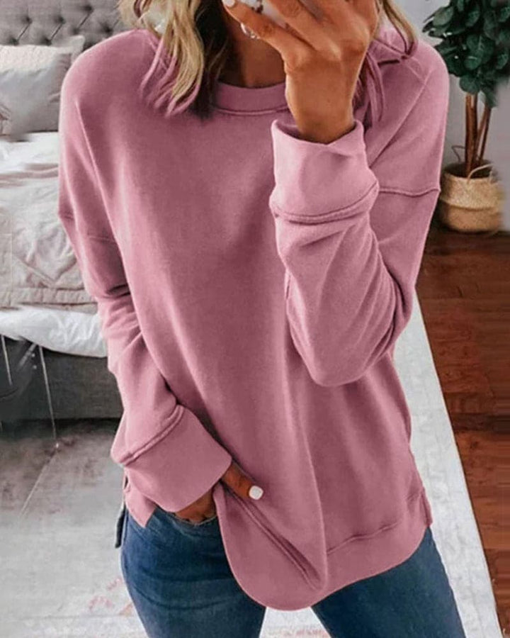 Three quarter view of a model wearing a pink oversized crew-neck sweatshirt with a rounded hem and side split