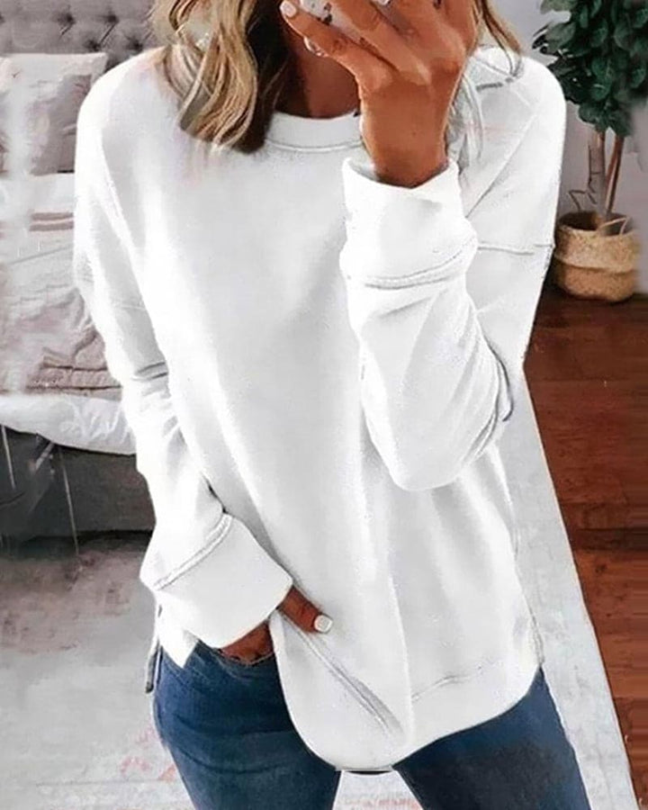 Close up view of a model wearing a white oversized crew-neck sweatshirt with a rounded hem and side split detail