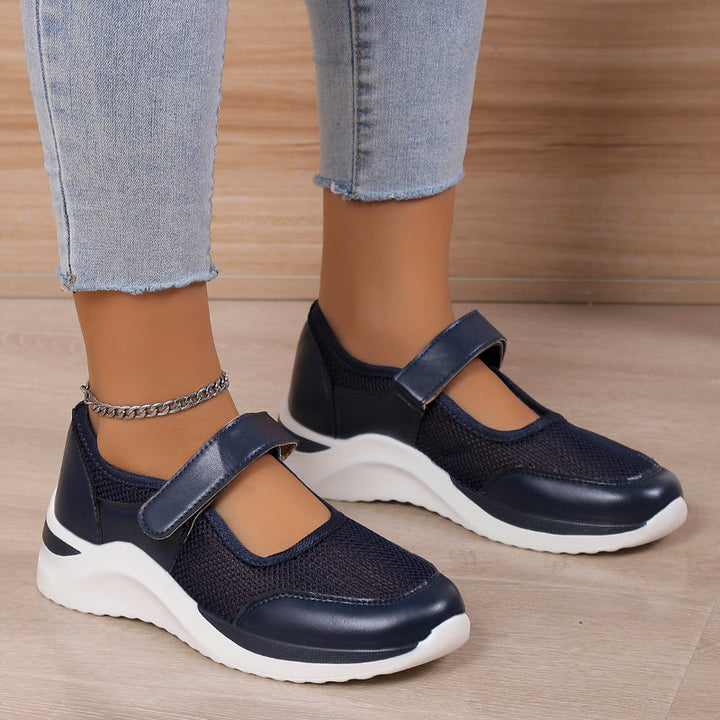 Side view of navy blue orthopedic Mary Jane shoes with mesh and white soles on a model wearing light blue jeans