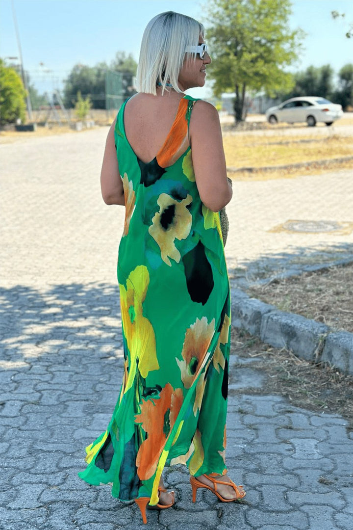 Back view of model wearing a green floral silk chiffon maxi dress with a deep U-neckline and orange heels