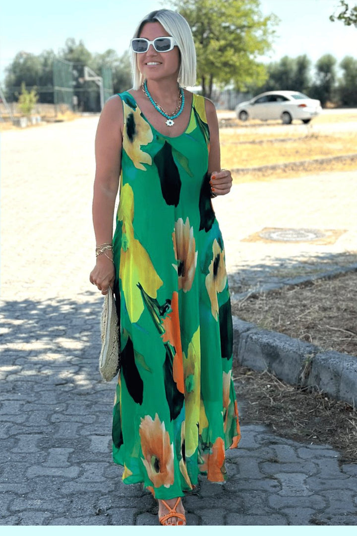 Front view of model wearing a green floral silk chiffon maxi dress, white sunglasses and a turquoise necklace