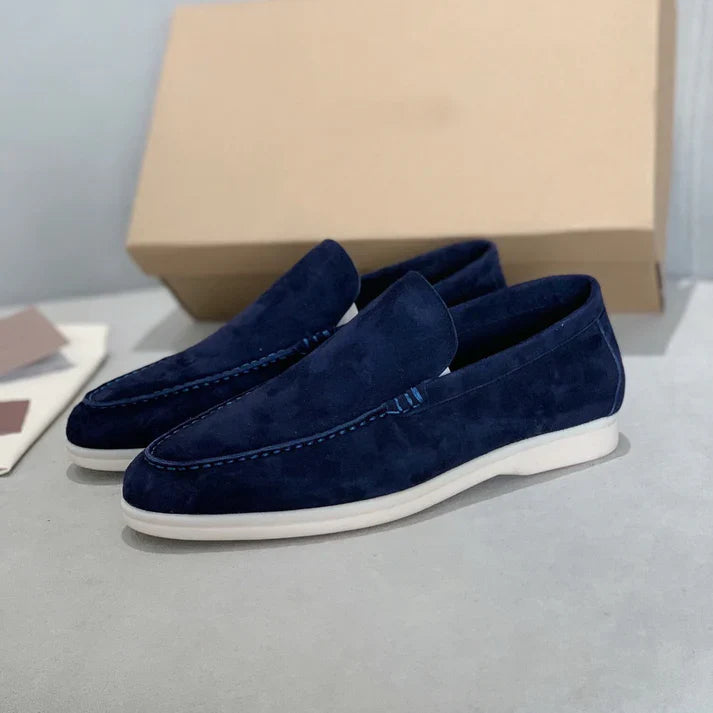 Back view of two navy suede loafers with white soles, a shoe box in the background