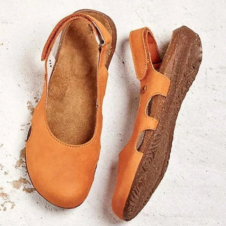 Back view of a pair of orange orthopedic sandals with cutouts and slingback straps on a white surface
