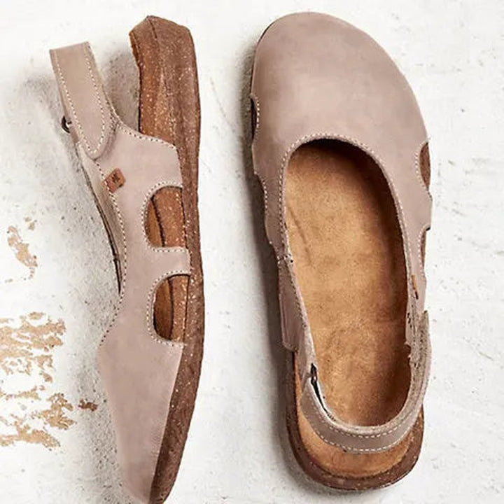 Top down view of a pair of beige orthopedic sandals with cutouts and slingback straps on a white surface